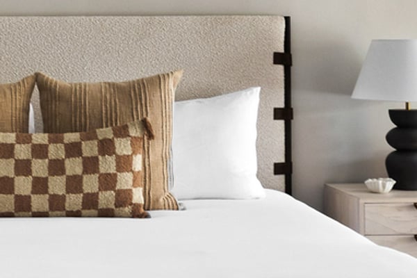 Bed with white linens, patterned throw pillows, and upholstered headboard next to nightstand with lamp