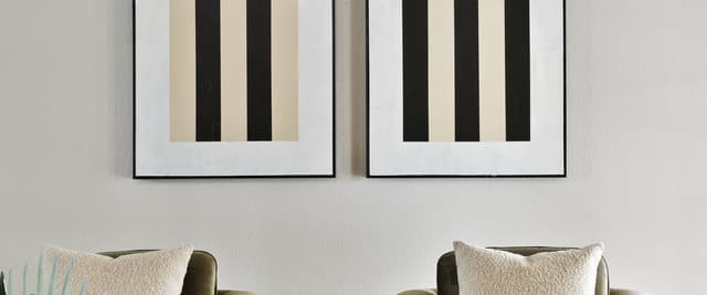 Two framed geometric prints with black and beige checkerboard patterns above olive-green armchairs with cream pillows