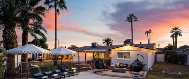 Backyard with illuminated mid-century home, pool, lounge chairs, white tent, and palm trees at sunset