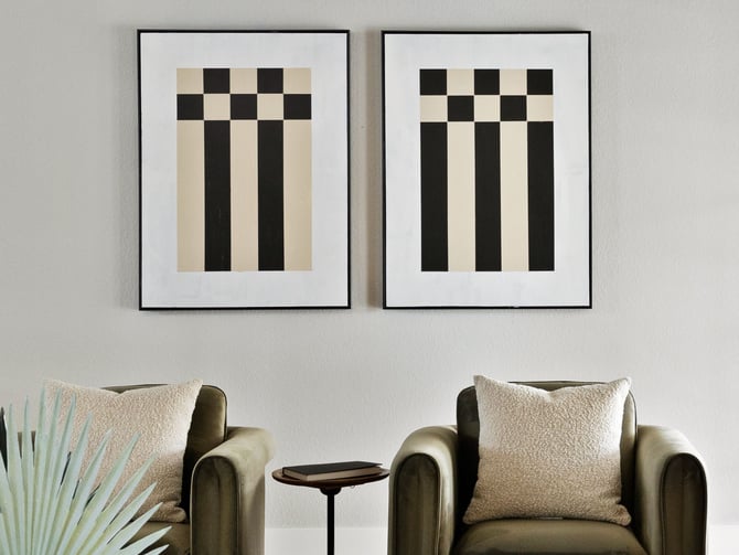 Two framed geometric prints with black and beige checkerboard patterns above olive-green armchairs with cream pillows