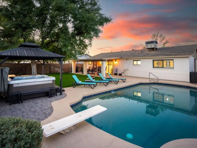 Backyard with swimming pool, hot tub under gazebo, lounge chairs, and illuminated house at sunset