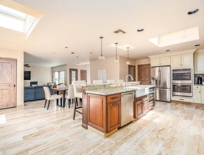 Open-plan kitchen and dining area with large island, stainless steel appliances, cream cabinetry, and skylights